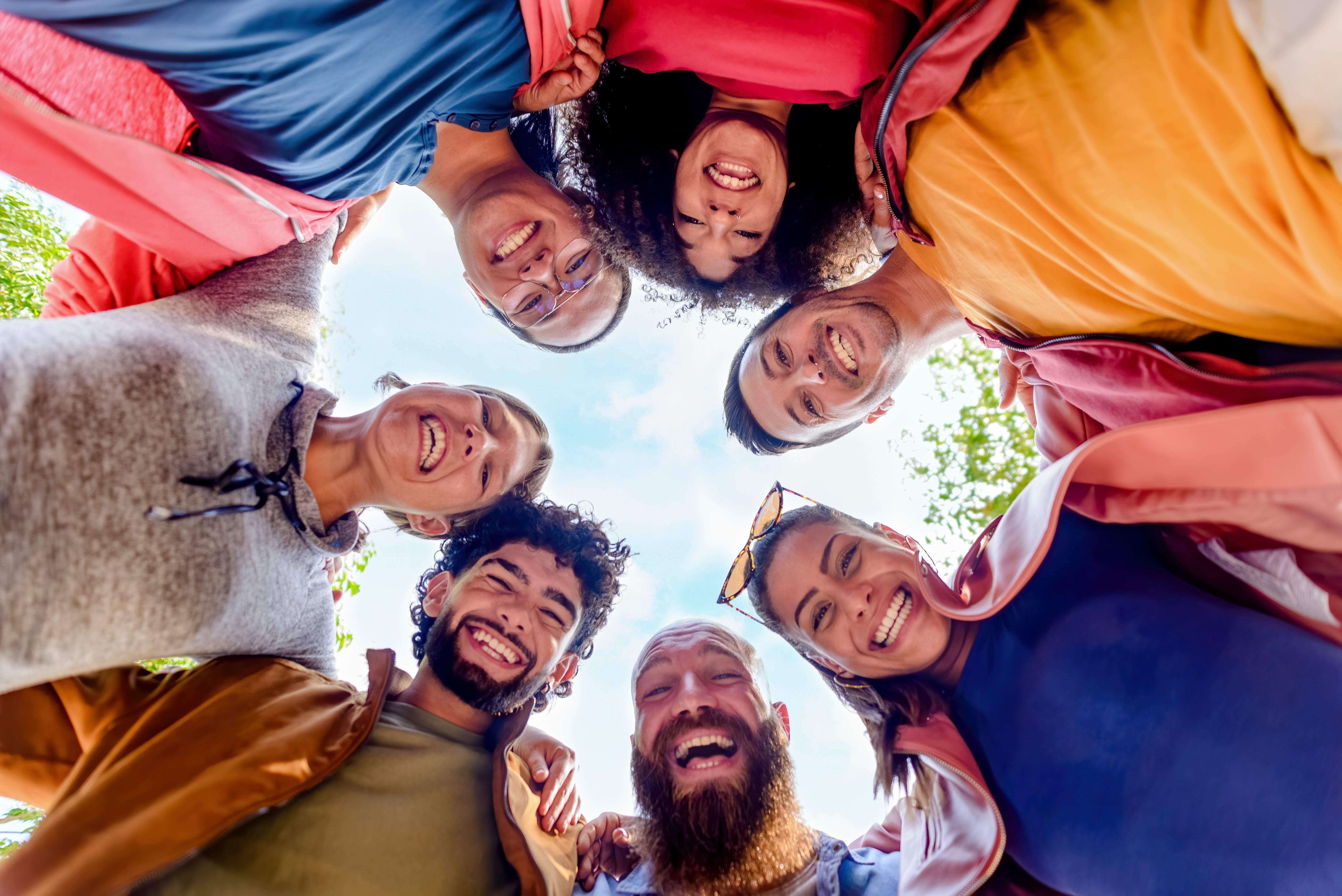 A group of diverse friends standing in a circle, smiling and looking down at the camera from below.