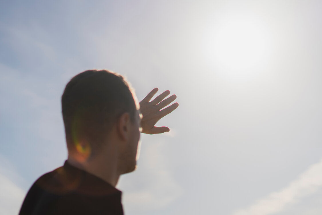 Man shielding his eyes with his hand while looking toward the bright sun, emphasizing the importance of sun protection and UV awareness.