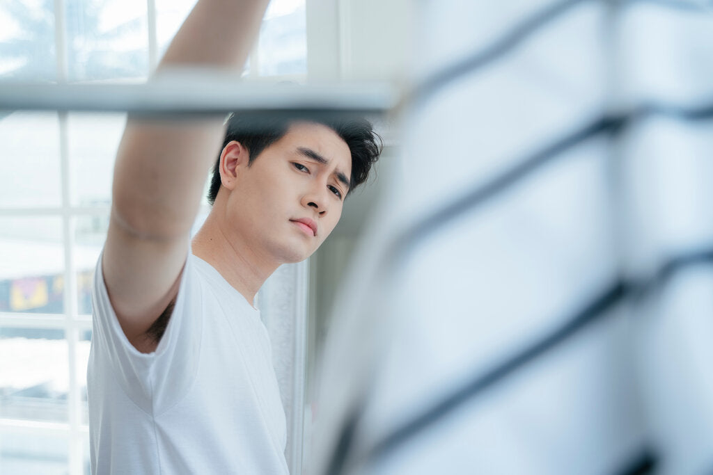 Young man in a white shirt inspecting his UPF clothing on a drying rack, thoughtfully checking the quality and wear of the fabric as sunlight streams through the window.