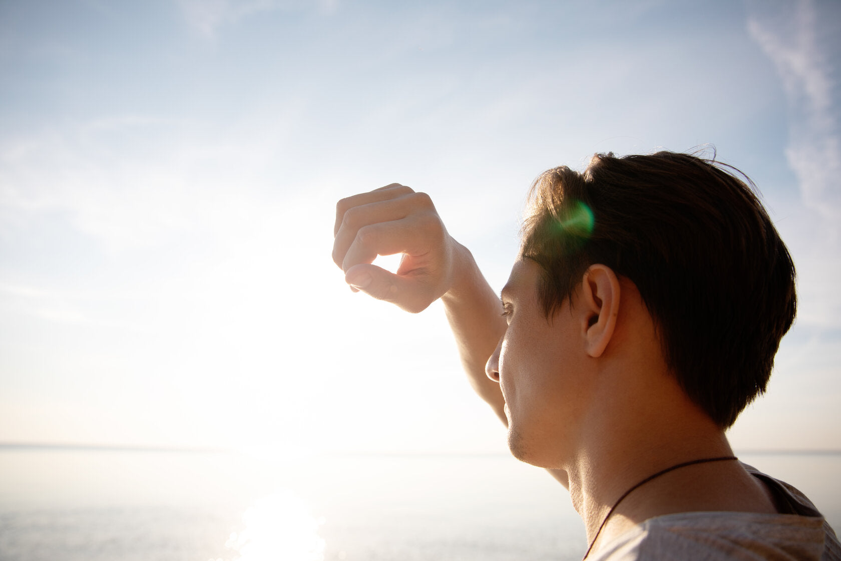 A man shielding his eyes from the bright sun while looking out over the water.