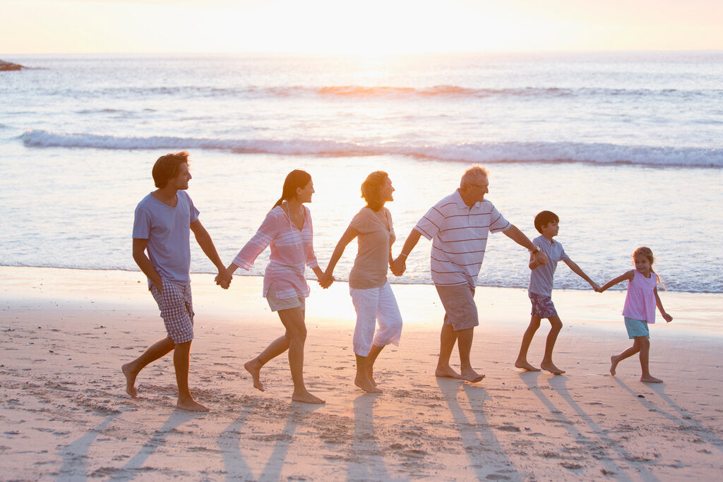 A multigenerational family walking hand in hand along the beach at sunset, with gentle waves in the background.