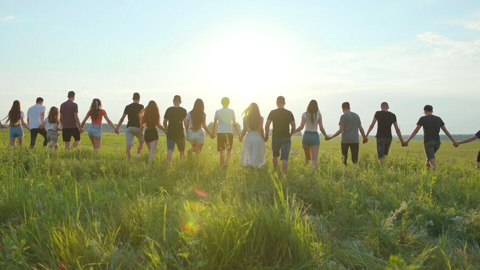 A group of people holding hands while walking through a sunny green field, symbolizing unity and togetherness under the bright sky.