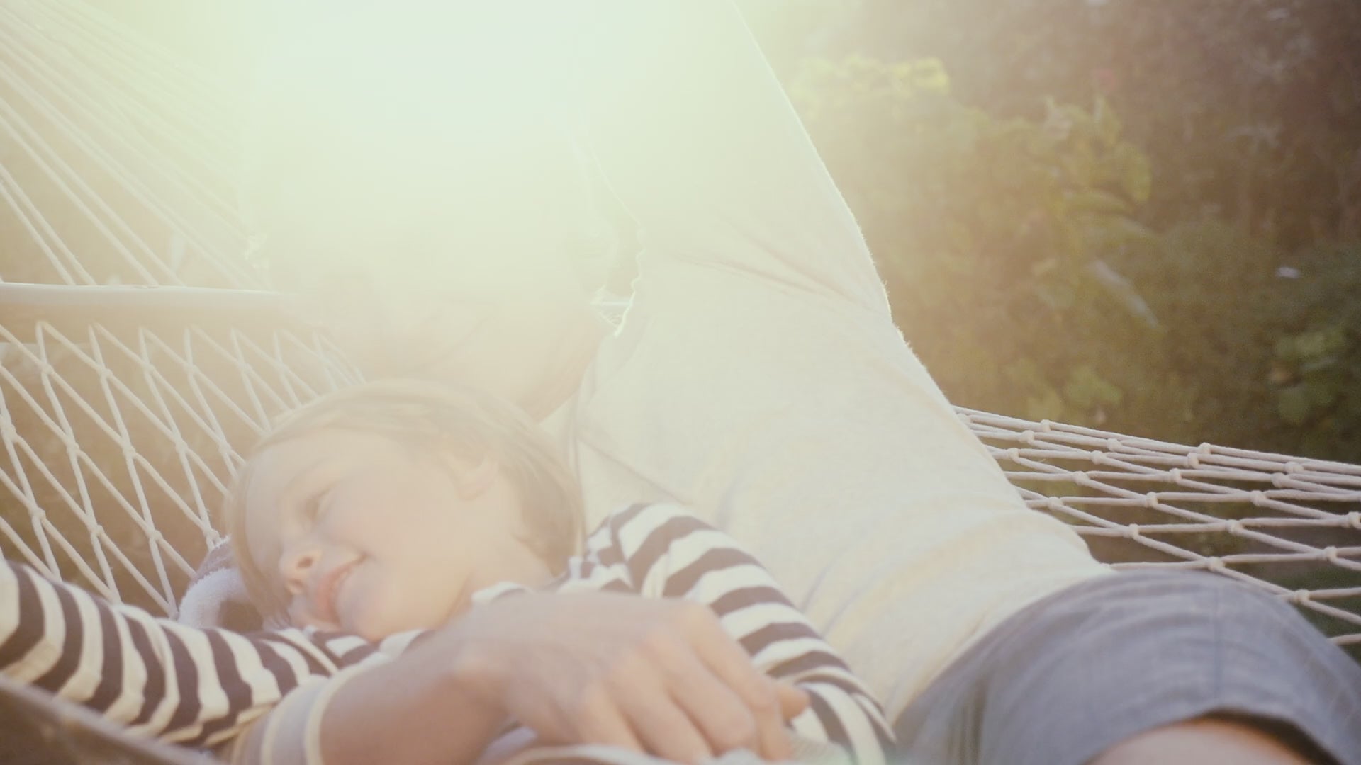 Adult and child relaxing on a hammock outdoors on a sunny day, smiling and enjoying the moment