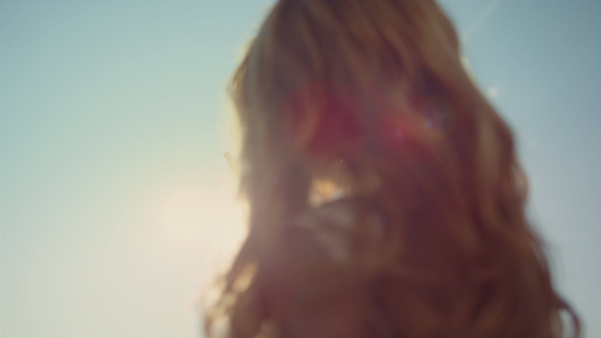 Woman reaching hand towards the sun in a clear sky, with sunlight creating a glowing effect